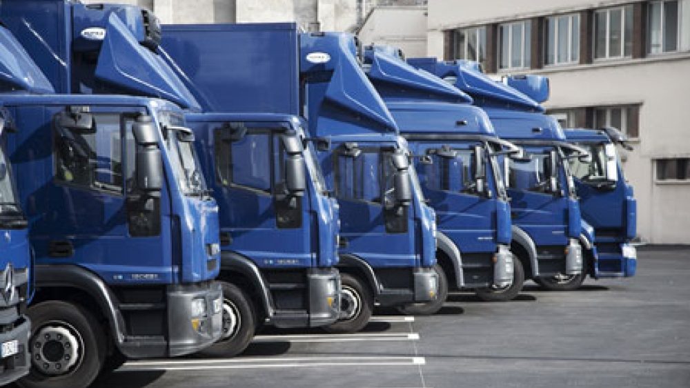 Fila de caminhões azuis de transporte de obras de arte estacionados no pátio da empresa