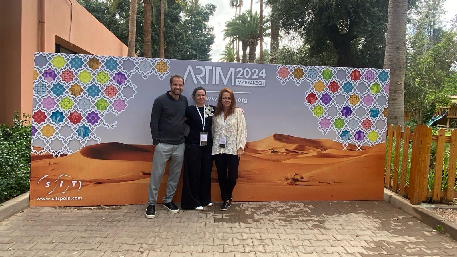 Três profissionais posam diante do painel do encontro ARTIM 2024, em Marrakesh